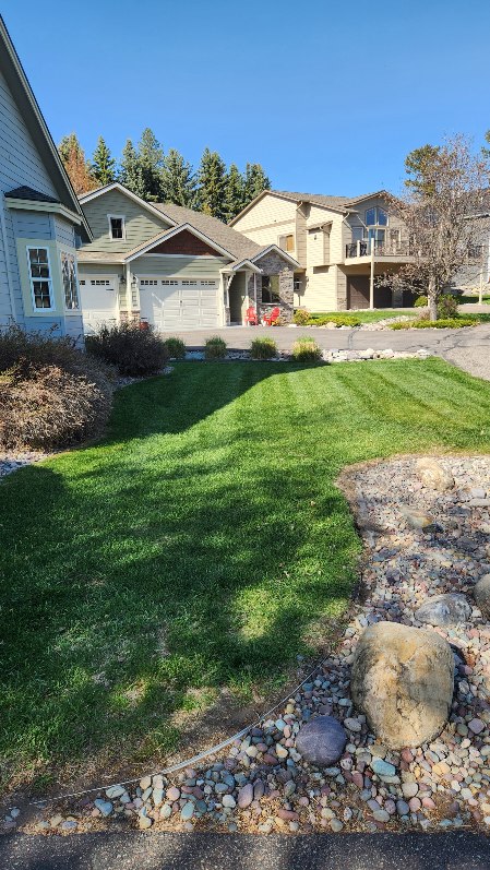 Front yard landscape bed with mulch, river rock, and a striped lawn mowing pattern