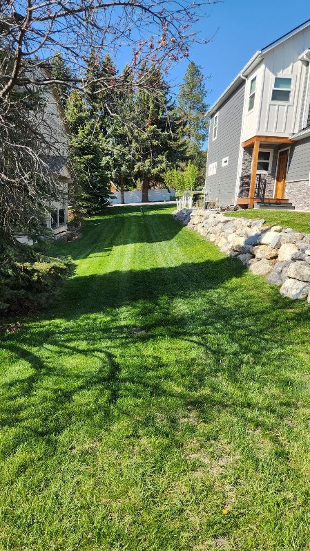 Sloped backyard lawn with a stacked boulder retaining wall beside a modern home